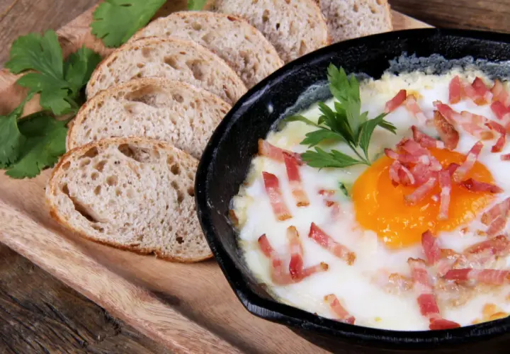 Un délicieux oeuf cocotte, parsemé de lardons croustillants, servi avec des tranches de pain de campagne.