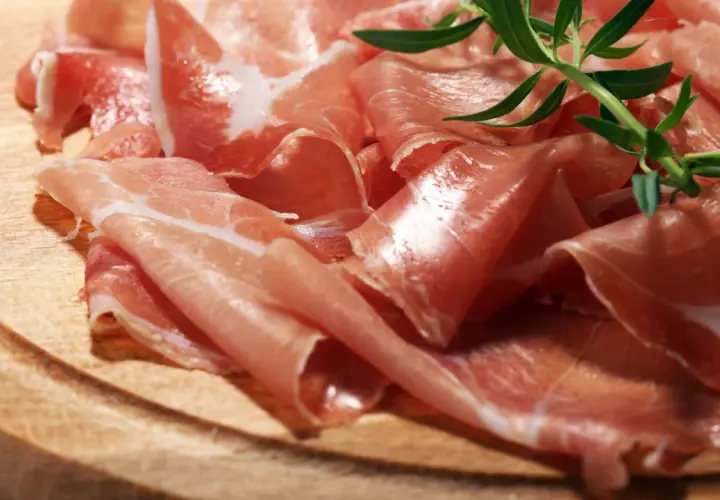 Cienkie plastry prosciutto crudo, ułożone na drewnianej desce, z gałązką rozmarynu. Pyszne, prawda?
