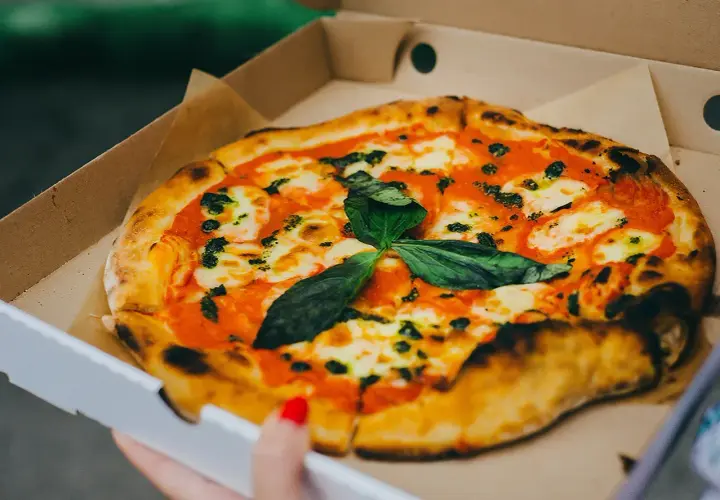 Pyszna pizza w kartonie na pizze, z sosem pomidorowym, mozzarellą i świeżą bazylią. Idealna na wynos!