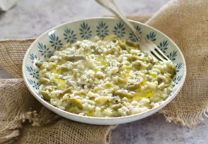 Un cremoso risotto con fagiolini, condito con olio d'oliva e pepe nero, servito in una ciotola decorata.