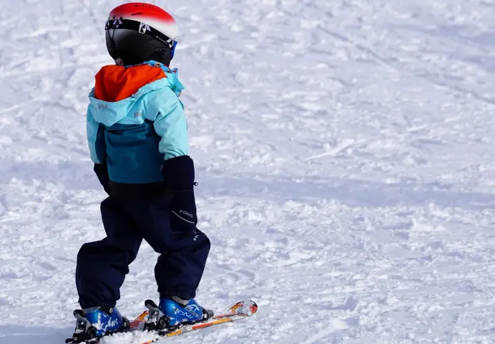 Bambino con casco, giacca e pantaloni da sci, pronto per sciare. Ecco cosa portare sulla neve per divertirsi in sicurezza!