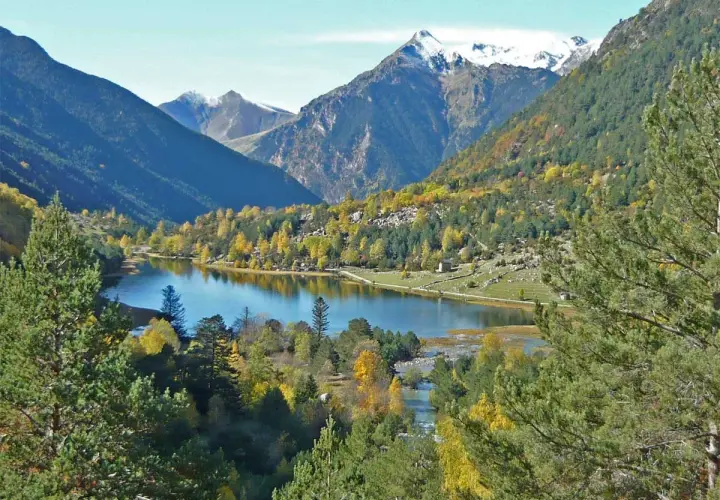 El estany de Llebreta, un lago alpino rodeado de bosques otoñales y montañas nevadas, ofrece una vista serena y colorida.