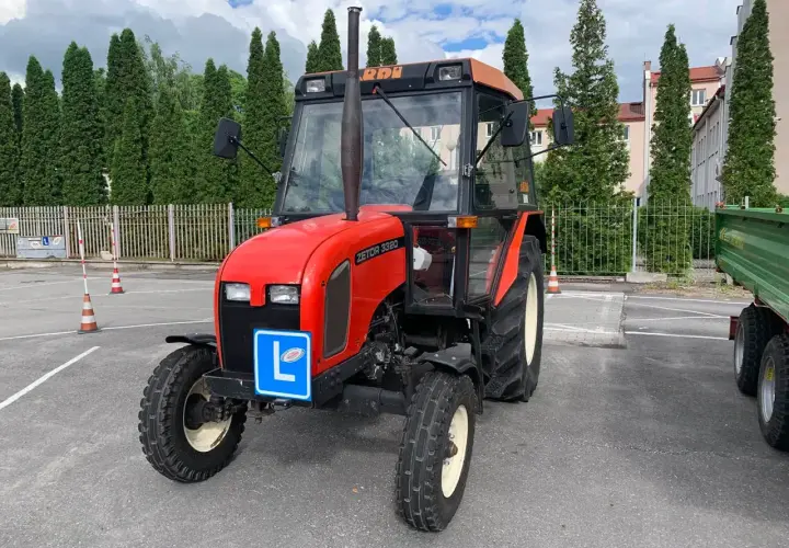 Czerwony traktor Zetor z literą "L" na niebieskiej tablicy, symbolizujący naukę jazdy. Kategoria t prawo jazdy.