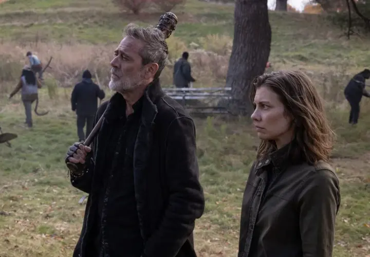 Maggie et Negan, le regard lointain, se tiennent côte à côte dans un paysage automnal. D'autres survivants travaillent en arrière-plan.