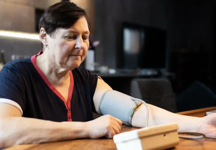 Kobieta w średnim wieku mierzy ciśnienie. Dba o prawidłowe ciśnienie tętnicze u 50-latka, monitorując je w domu.