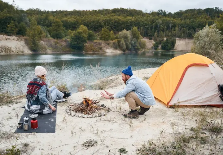 Para spędza wakacje pod namiotem nad jeziorem, rozpalając ognisko.