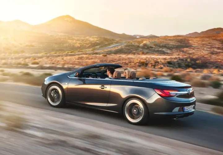 Para podróżuje kabrioletem Opel Cascada przez pustynny krajobraz o zachodzie słońca.