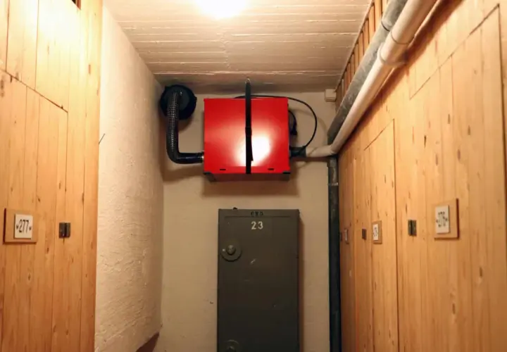 Röd radonfläkt monterad på väggen i en källarkorridor med träpaneler. En ventilationstrumma leder bort luften.