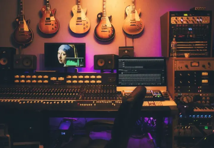 Guitars suspendus au-dessus d'une console de mixage, d'écrans et de racks d'équipement studio d'enregistrement, baignant dans une lumière violette.