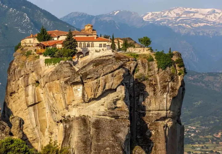 Monastery perched atop a massive rock formation in Meteora, Greece. The ancient stone buildings with red-tiled roofs seem to defy gravity, offering a glimpse into timeless Meteora hours.