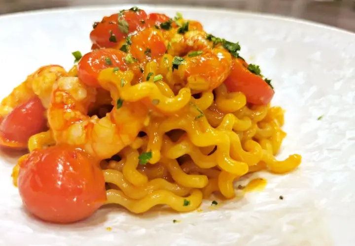 Un piatto invitante di pasta con gamberetti, pomodorini succosi e un tocco di prezzemolo fresco.