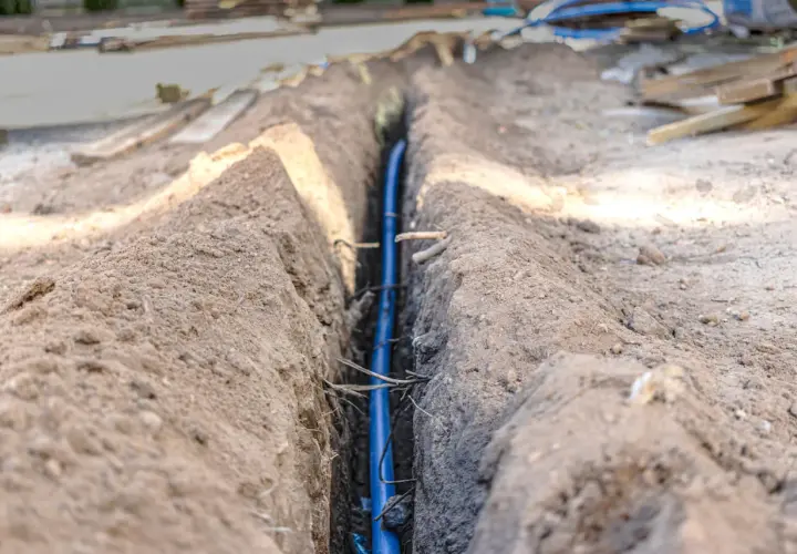 Wykopany rów z niebieską rurą, prawdopodobnie na jakiej głębokości kabel elektryczny zostanie ułożony.