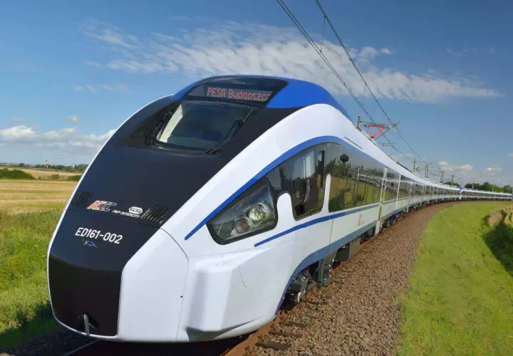 Nowoczesny pociąg Pesa Bydgoszcz ED161-002 mknie po torach wśród pól i zieleni, pod błękitnym niebem z chmurami.