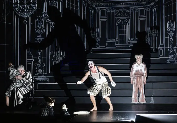 Scen från "Misantropen" på Dramaten. En clownliknande figur, en kvinna i randigt och en äldre kvinna i rosa pyjamas.