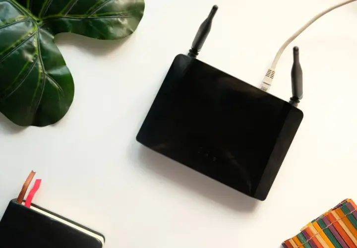 Czarny router z antenkami i kablem. Obok liść, notatnik i kolorowa podkładka. Czy router pobiera dużo prądu?