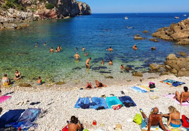 Plage de galets à Terrasini, Sicile. Des baigneurs profitent de l'eau cristalline sous un soleil radieux.