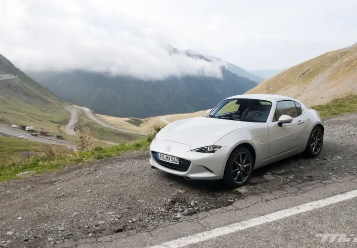Un Mazda MX5 blanco en una carretera de montaña. Las opiniones sobre este coche son muy positivas, ideal para disfrutar de paisajes así.