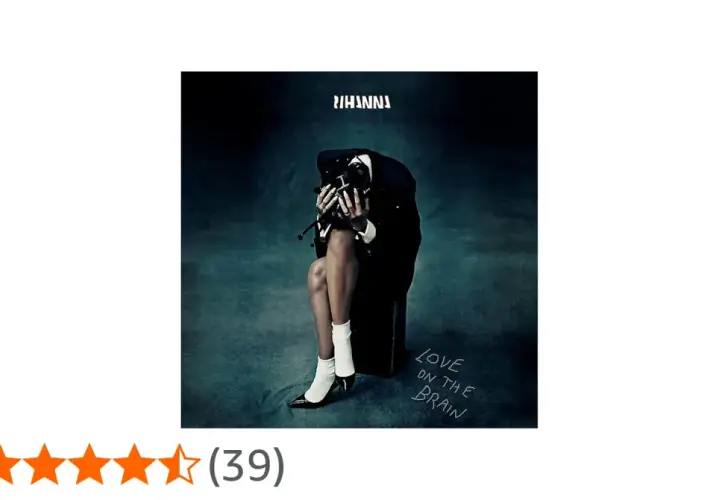 Rihanna w czarnym garniturze, siedząca z głową opuszczoną na dłonie, na tle mrocznego gradientu.