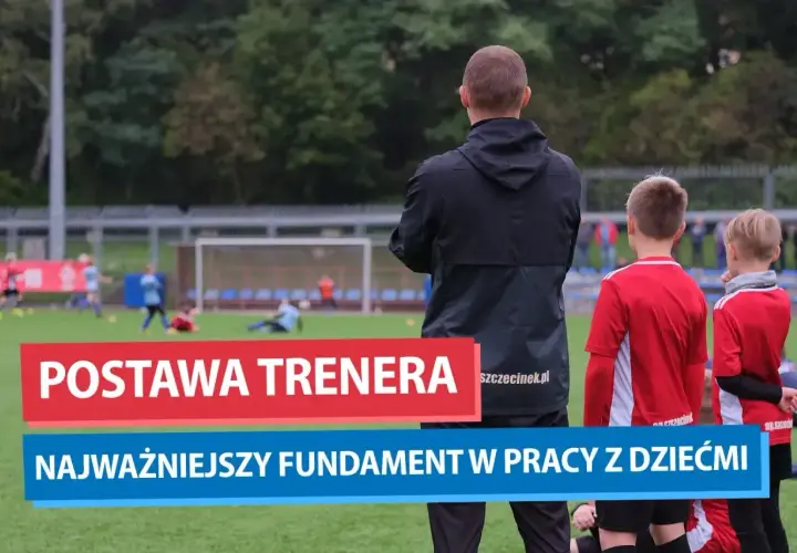 Trener motywacyjny obserwuje młodych piłkarzy na boisku. Jego postawa to fundament pracy z dziećmi.