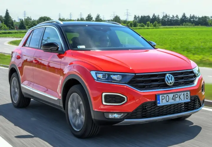 Czerwony volkswagen t-roc używany na drodze, z zielonym polem w tle.