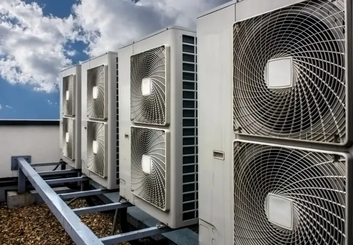 Rząd jednostek klimatyzacyjnych na dachu pod błękitnym niebem z chmurami.