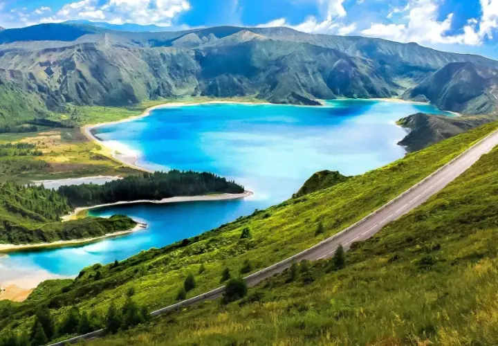 Carretera serpenteante en una ladera verde con lagos azules y montañas al fondo, un paisaje idílico de Portugal en octubre.