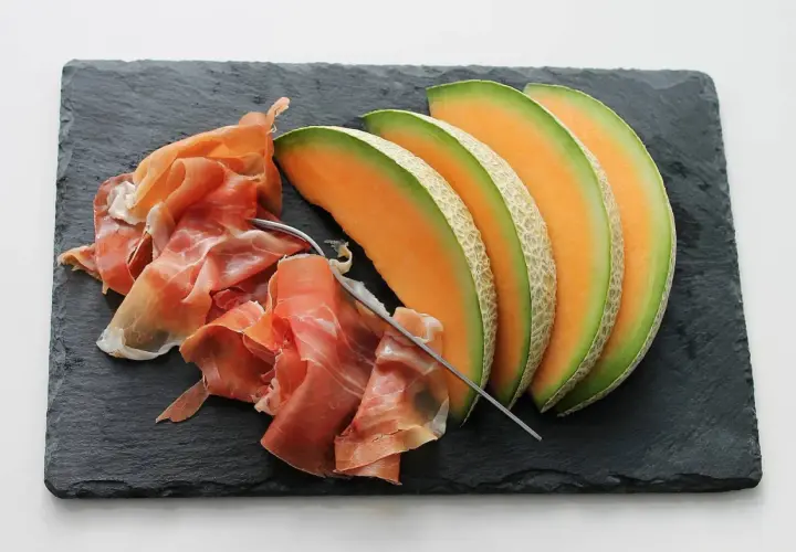 Tranche de melon et jambon cru sur ardoise. Quel vin avec melon et jambon cru ? Un vin blanc sec et fruité ou un rosé léger serait parfait.