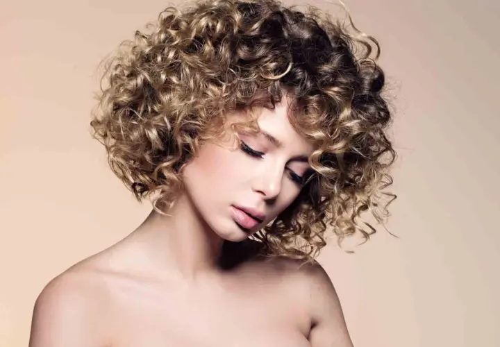 Mujer con un moderno bob cortes de pelo rizado, con reflejos rubios y castaños, mirada serena.