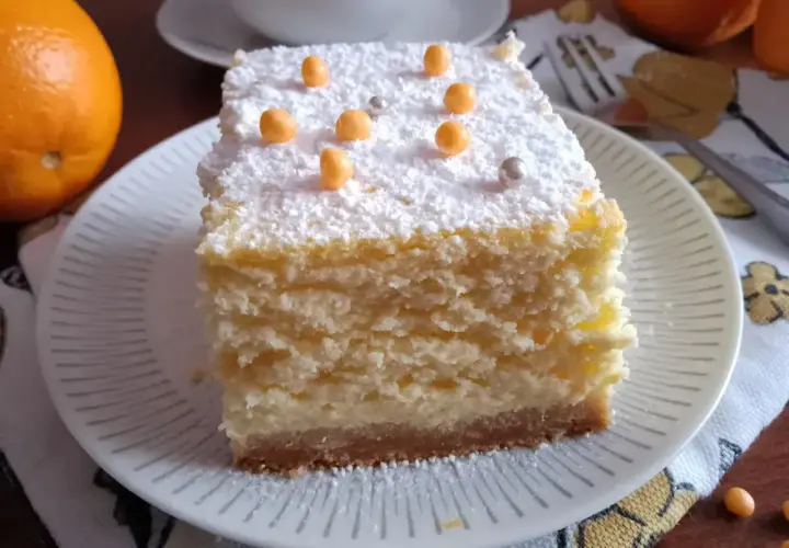 Pyszny sernik pieczony z delikatnym spodem z herbatników, posypany cukrem pudrem i pomarańczowymi kuleczkami.