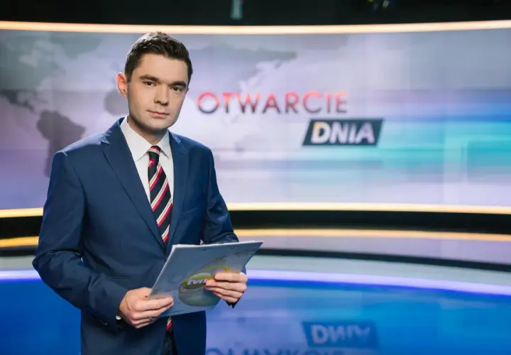 Jan Niedziałek, dziennikarz w garniturze, trzyma dokumenty w studiu telewizyjnym z napisem "OTWARCIE DNIA".