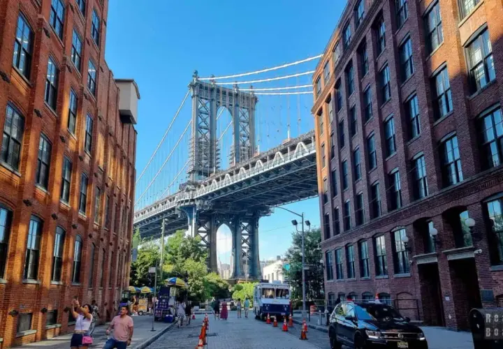 Ulica w **brooklyn** z ceglanymi kamienicami i majestatycznym mostem w tle.
