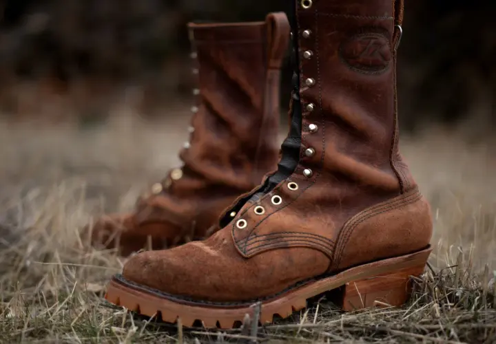 Two brown leather work boots with a lug sole, meaning a thick, rugged sole with deep treads for excellent grip, stand in dry grass.
