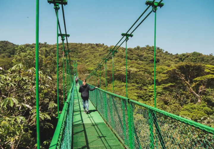 Frauen spazieren über eine Hängebrücke im Regenwald von Monteverde, Costa Rica, mit üppiger grüner Vegetation.
