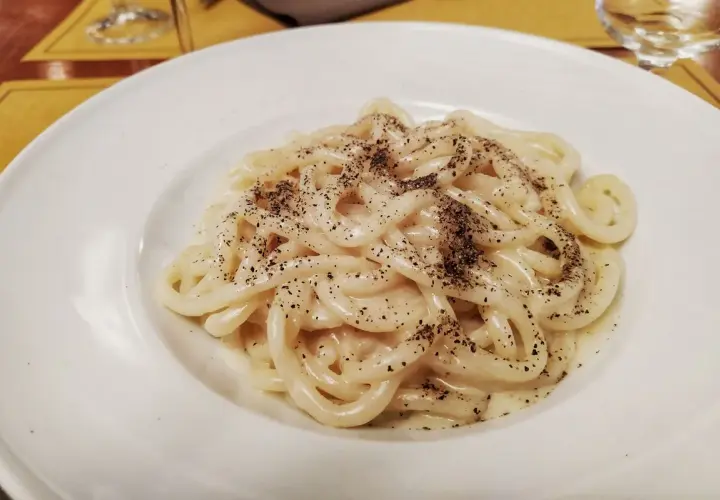 Pici cacio e pepe, un classico piatto romano, servito in un piatto bianco.
