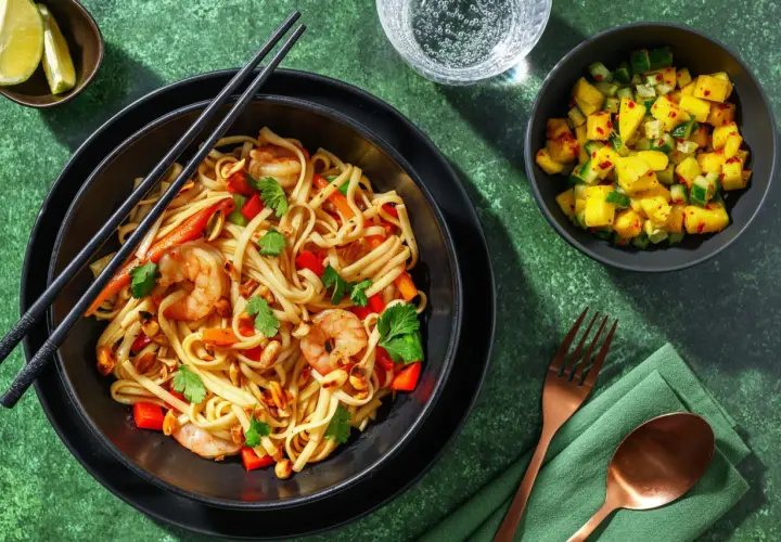 En skål med nudlar, räkor, paprika och jordnötter, perfekt för ett snabbt pad thai recept. Serveras med en mangosallad och limeklyftor.