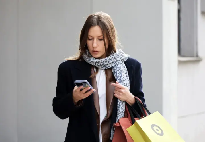 Kobieta w granatowym płaszczu i wzorzystym szaliku trzyma telefon. Czyżby szukała informacji, jaki kolor jest teraz modny?