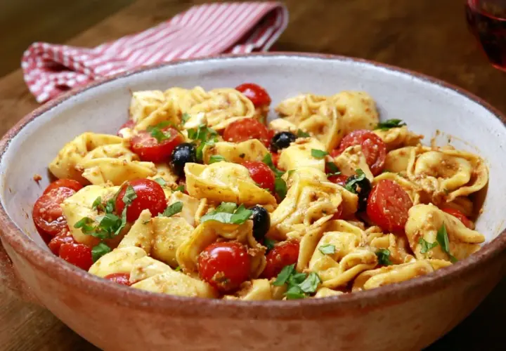 Herzhafter Tortellini Salat mit Kirschtomaten, schwarzen Oliven und frischem Basilikum in einer rustikalen Schüssel.