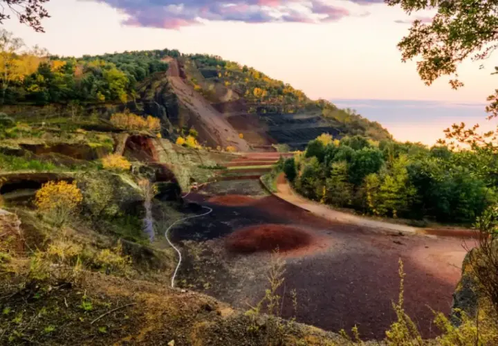 Paisaje del parc natural de la zona volcànica de la Garrotxa con laderas escalonadas, vegetación otoñal y el cielo rosado del atardecer.
