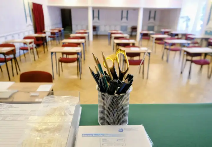 Przygotowania do matury z angielskiego: ołówki, nożyczki i zeszyty czekają na uczniów w pustej sali egzaminacyjnej.