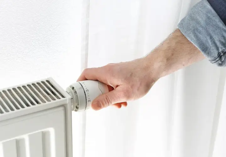 Dłoń reguluje termostat grzejnika, próbując obniżyć zbyt wysoką temperaturę w domu.