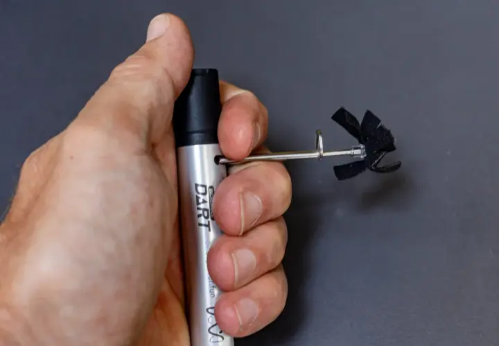 A hand holds a silver "DART" marker with a small, black, propeller-like attachment. This is part of a stans dart review.