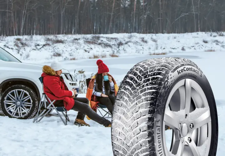 Ett par njuter av en paus i snön bredvid en bil, med en vinterdäck i förgrunden. Välj dubb eller dubbfritt för din trygghet.