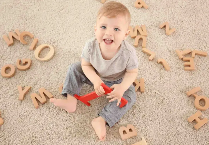 Bambino sorridente circondato da lettere di legno, un modo divertente per iniziare a capire come sviluppare il linguaggio nei bambini.