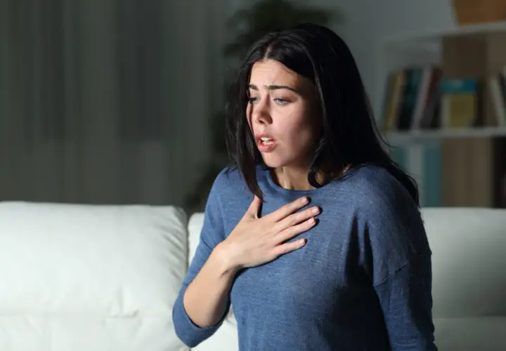 Donna con mano sul petto, respiro affannoso, espressione di chi soffre di attacchi di ansia.