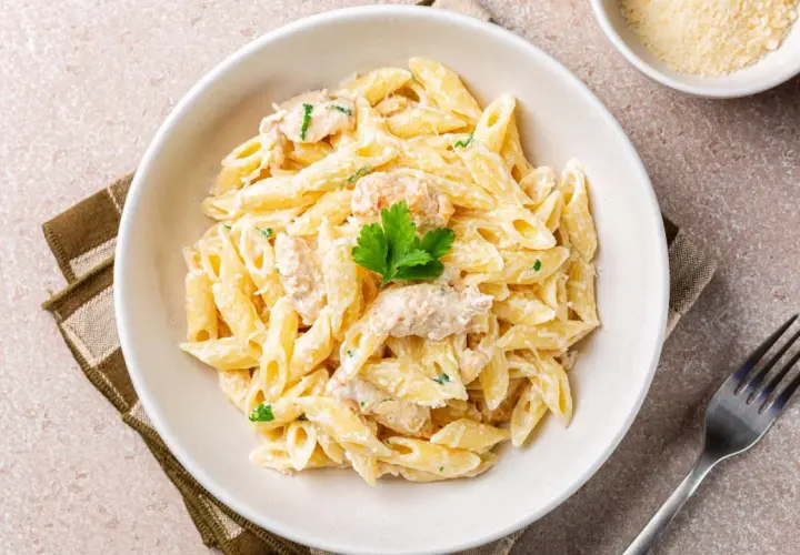 Penne w kremowym sosie, przypominające fettuccine alfredo, z kawałkami kurczaka i natką pietruszki.