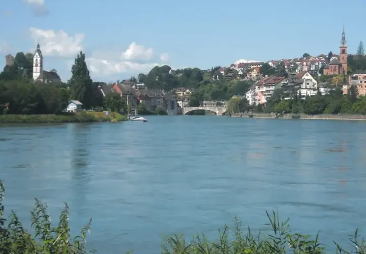Un río azul fluye hacia una ciudad con iglesias y casas en la ladera, parte de la ruta EuroVelo 15.