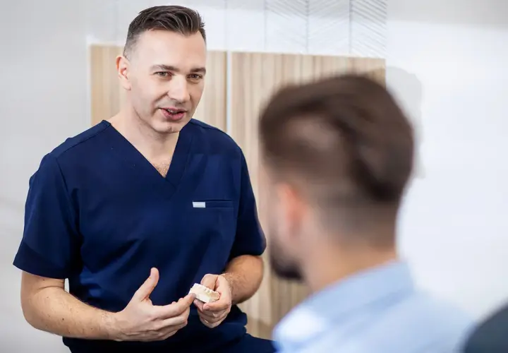 Dentysta w granatowym uniformie pokazuje pacjentowi model szczęki.