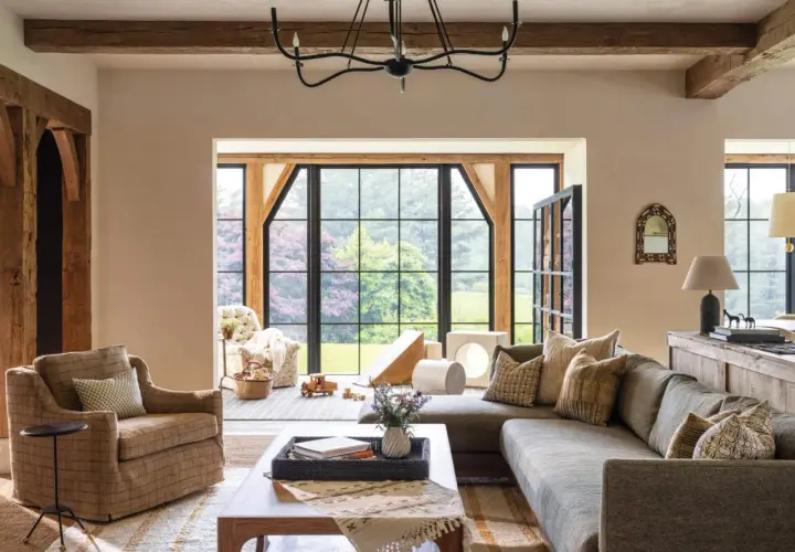 A cozy living room with exposed wooden beams, a large sectional sofa, and a plaid armchair, embodying rustic chic interior design.