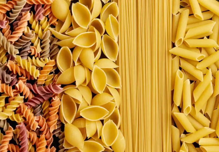 Różne rodzaje makaronu: kolorowe fusilli, muszelki, spaghetti i penne. Wybór wpływa na indeks glikemiczny posiłku.