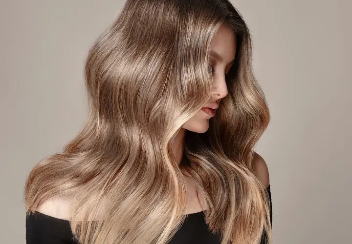 Mujer con cabello largo y ondulado en tonos castaños y rubios, ideal para quienes buscan cómo quitar el tinte del cabello y dejarlo natural.